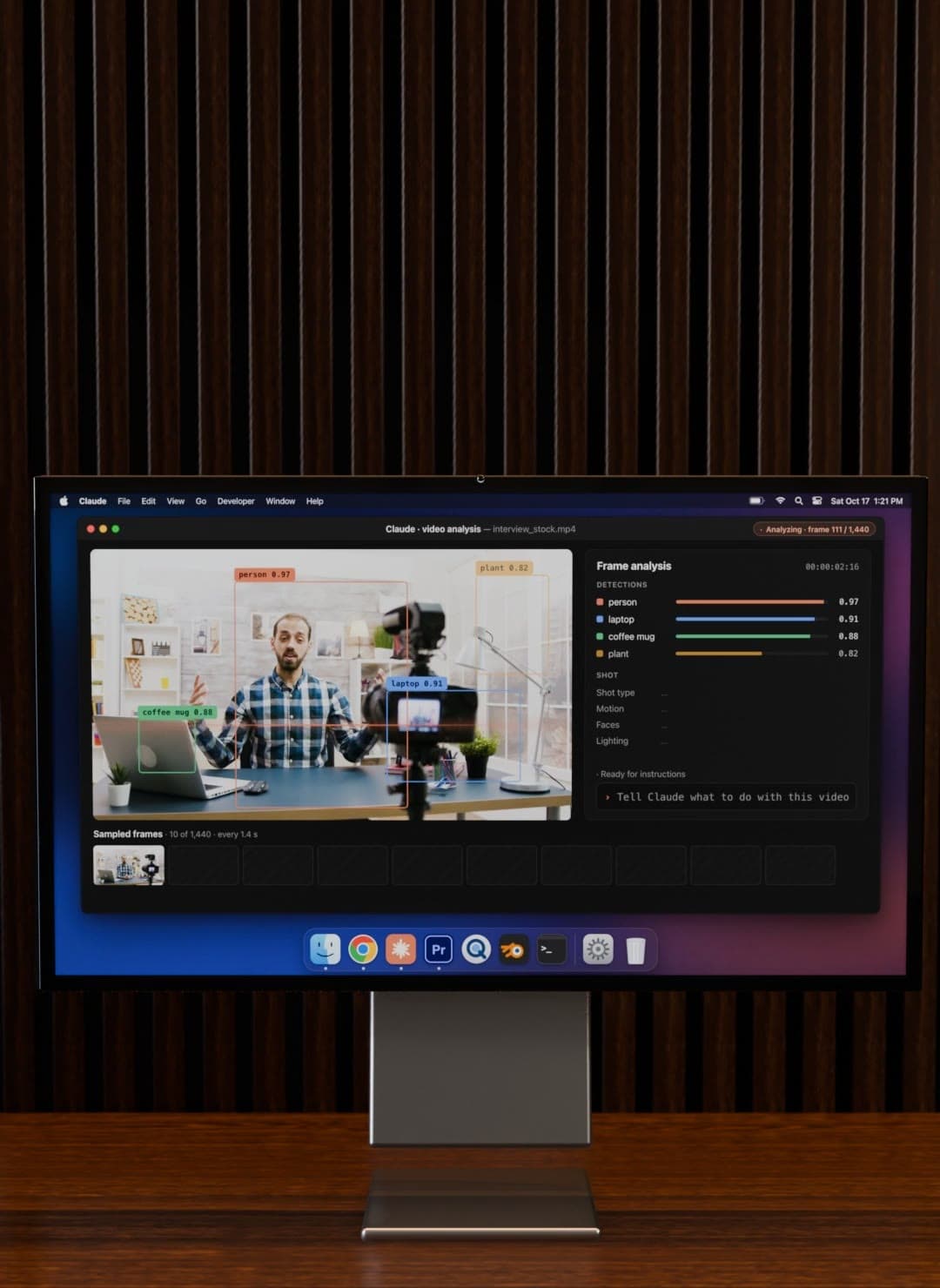 A Studio Display on a walnut desk showing a Claude video analysis window, with labelled detection boxes around a person, a laptop, a coffee mug and a plant.